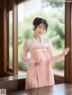 A woman in a pink hanbok standing by a window.