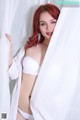 A woman with red hair wearing a white bra and panties.