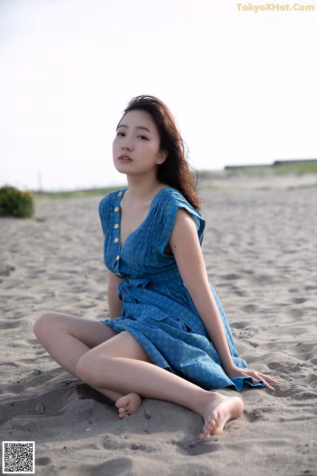 A woman in a blue dress sitting on the sand.