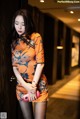A woman in an orange dress leaning against a wall.