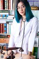 A woman with blue hair and glasses sitting at a desk.